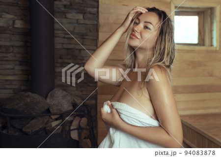 A young woman relaxes and sweats in a hot sauna wrapped in a towel. girl in the sauna. Finnish sauna interior, classic wooden sauna with hot steam. Russian bath. A young woman relaxes and sweats in a hot sauna wrapped in a towel. girl in the sauna. Finnish sauna interior, classic wooden sauna with hot steam. Russian bath. 94083878