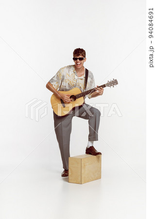 Portrait of young ma in sunglasses playing guitar, posing isolated over white studio background. Looks happy 94084691