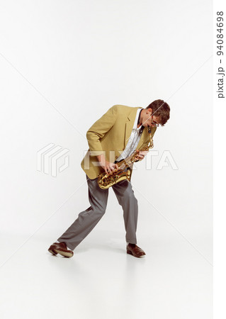 Portrait of young man in stylish yellow jacket playing saxophone isolated over white background. Vintage music 94084698