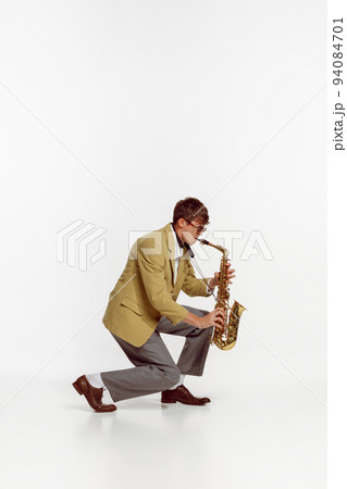 Portrait of young man in stylish yellow jacket playing saxophone isolated over white background. Expressive music 94084701