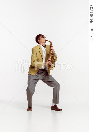 Portrait of young man in stylish yellow jacket playing saxophone isolated over white background. Jazz performer 94084702