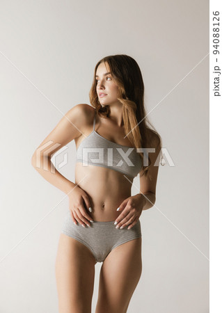 Studio shot of young charming slim girl in grey cotton underwear isolated over gray background. Wellness, fitness, diet, fashion, natural beauty of female body Studio shot of young charming slim girl in grey cotton underwear isolated over gray background. Wellness, fitness, diet, fashion, natural beauty of female body 94088126