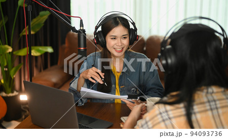 Two young female bloggers in headphones looking and talking each other while recording conversation, interview for their channel 94093736