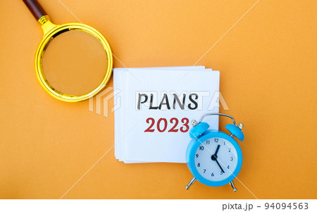 Note with words Plans 2023. Setting goals and planning targets for the next year. Motivation, vision. Business and finance concept. Magnifying glass and alarm clock 94094563