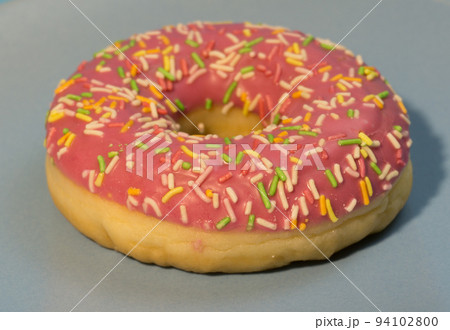 Pink doughnut or donut with colored sprinkles on a blue background. Bitten off American bagel. Pink doughnut or donut with colored sprinkles on a blue background. Bitten off American bagel. 94102800