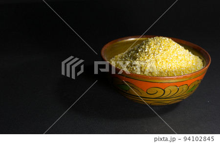 Raw corn grits in a wooden bowl on a black background Raw corn grits in a wooden bowl on a black background 94102845