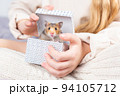 A cute fluffy golden hamster looks out of a gift box in the hands of a girl in knitted home clothes and looks at camera. Beautiful postcard with an animal theme. Pet as a gift for birthday, christmas. 94105712