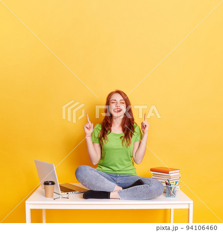 Young ginger overjoyed woman with red hair, wears jeans and green t shirt, points with both index finger upwards, shows free space for your advertising content, winking and showing tongue. Young ginger overjoyed woman with red hair, wears jeans and green t shirt, points with both index finger upwards, shows free space for your advertising content, winking and showing tongue. 94106460