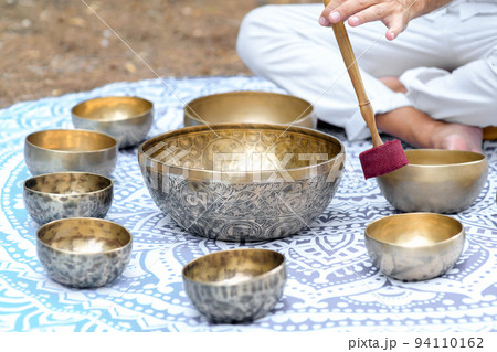 Close-up of man hands playing on a singing tibetian bowl with sticks. Sound healing music instruments for meditation 94110162