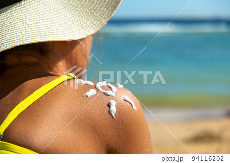 Back view of young woman tanning at the beach with sunscreen cream in sun shape on her shoulder. UV sunburn protection and sunblock skincare concept Back view of young woman tanning at the beach with sunscreen cream in sun shape on her shoulder. UV sunburn protection and sunblock skincare concept 94116202