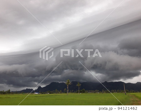 Gray Cumulonimbus cloud formations on sky above mountain, Nimbus moving with rice field,  Arcus cloud rolling in the storm with Appearance of rain cloud,  Meadow plant green while rain falling 94121462