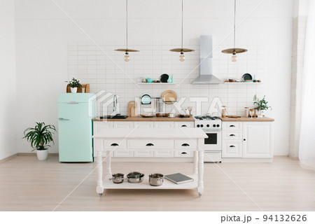 The bright Scandinavian-style kitchen features a mint-colored refrigerator. Wooden kitchen table with dishes 94132626