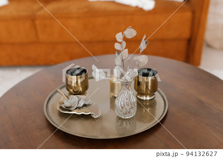 Gold glasses, dried flowers in a vase on a round tray on the coffee table 94132627