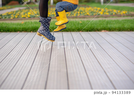 Feet in yellow rubber boots of a mother and son. Seasonality, seasons, fallen dry maple leaves 94133389