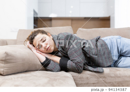 Young woman sleeping on sofa at home, tired after work Young woman sleeping on sofa at home, tired after work 94134387