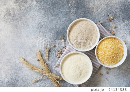 Food and baking gluten free ingredient. Cereals and flours coarse, corn flour, buckwheat flour, chickpeas flour over gray stone background. View from above. Copy space. Food and baking gluten free ingredient. Cereals and flours coarse, corn flour, buckwheat flour, chickpeas flour over gray stone background. View from above. Copy space. 94134388