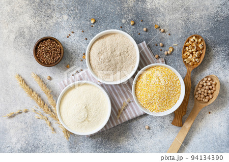 Food and baking gluten free ingredient. Cereals and flours coarse, corn flour, buckwheat flour, chickpeas flour over gray stone background. View from above. 94134390
