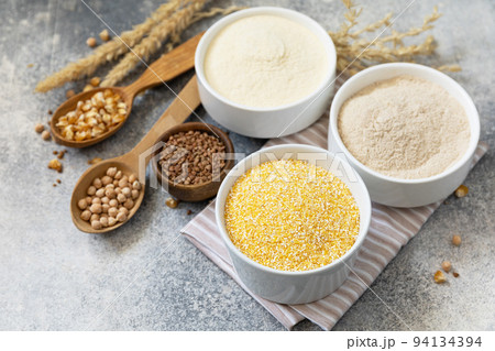 Food and baking gluten free ingredient. Cereals and flours coarse, corn flour, buckwheat flour, chickpeas flour over gray stone background. Copy space. 94134394