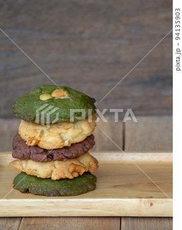 Multiple color cookies inclusive peanut butter, green tea cookies, and Chocolate Chip Cookies. Overlaid by alternating colors on wood plate. Multiple color cookies inclusive peanut butter, green tea cookies, and Chocolate Chip Cookies. Overlaid by alternating colors on wood plate. 94135903