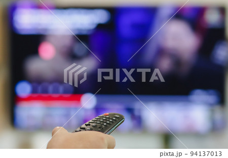 Close-up of hand with the remote control television and presses the button. Television remote control changes channels thumb on the blue TV screen. 94137013