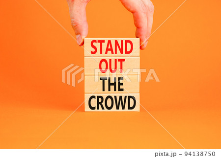 Stand out the crowd symbol. Concept words Stand out the crowd on wooden blocks on beautiful orange table orange background. Businessman hand. Business, stand out the crowd concept Stand out the crowd symbol. Concept words Stand out the crowd on wooden blocks on beautiful orange table orange background. Businessman hand. Business, stand out the crowd concept 94138750