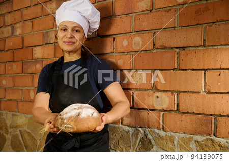 Happy woman baker entrepreneur holds loaf of bread, working at her artisanal family bakery store, selling homemade bread 94139075