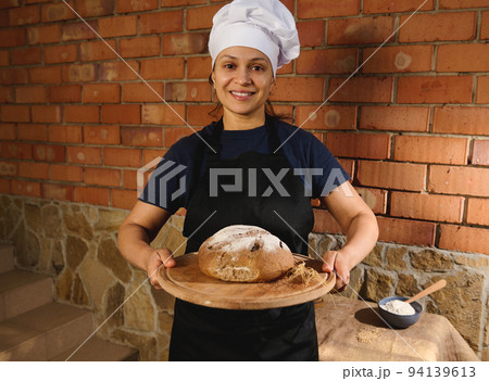 Beautiful Hispanic woman baker holds a wooden board with fresh homemade whole grains sourdough rye bread and wheat ears Beautiful Hispanic woman baker holds a wooden board with fresh homemade whole grains sourdough rye bread and wheat ears 94139613