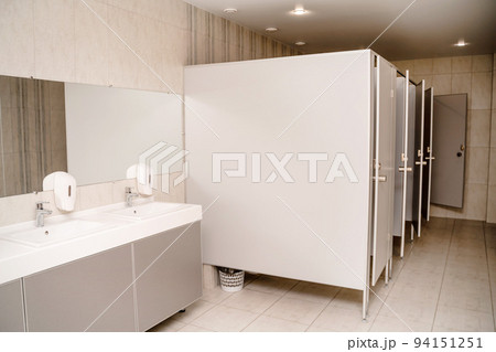 The interior of a public toilet. Row of wash basins with metal faucets on a marble slab, liquid soap dispensers, a long mirror on a gray wall 94151251