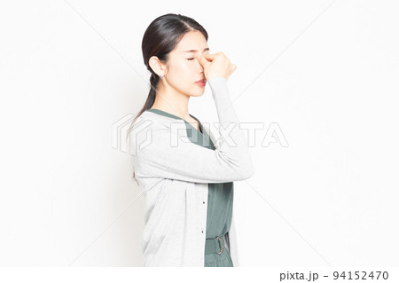 白背景の前に立って目頭をつまむ主婦 94152470