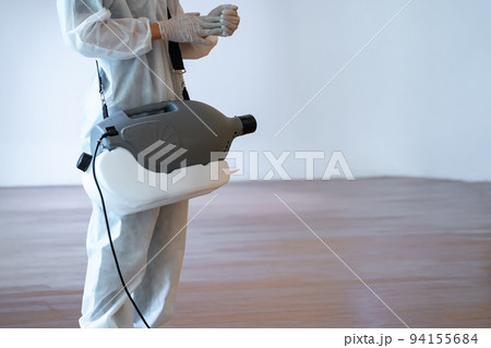 Professional technical man in prevention suit sprays sterilizing solution.by electrical prepares himself before spray machine on the wood floor and white background with studio light. 94155684