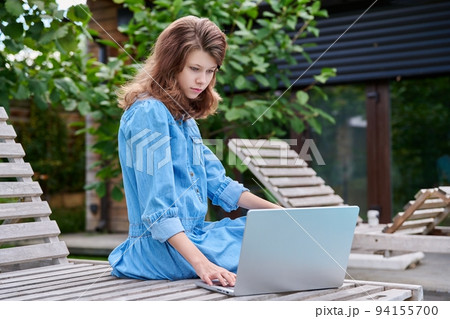 Teenage girl 12, 13 years old sitting with laptop in backyard Teenage girl 12, 13 years old sitting with laptop in backyard 94155700