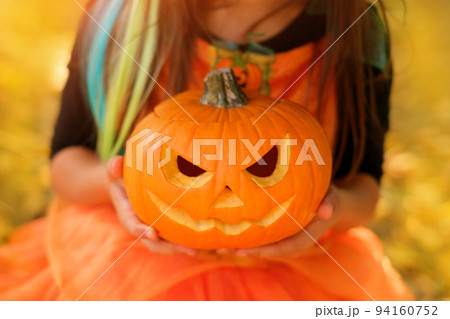 A child holds a pumpkin with a carved sinister smile in his hands at the sunset of the autumn sun. Traditions on Halloween. close-up A child holds a pumpkin with a carved sinister smile in his hands at the sunset of the autumn sun. Traditions on Halloween. close-up 94160752
