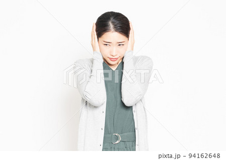 騒音に困って耳を塞いでいる女性 94162648