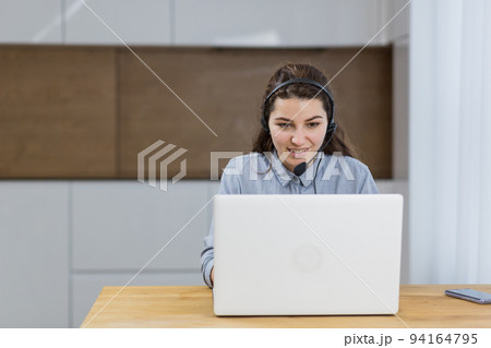 Young beautiful student girl studying at home online, remotely, with laptop in headphones, sitting at the table, smiling Young beautiful student girl studying at home online, remotely, with laptop in headphones, sitting at the table, smiling 94164795