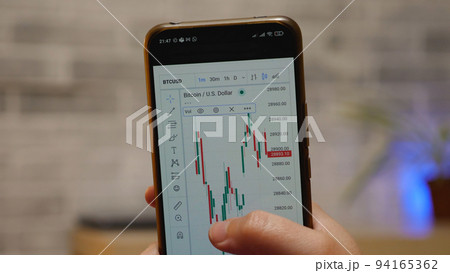 On the smartphone screen is a graph of the bitcoin cryptocurrency value in U.S. dollars. In the background is a light stone wall. BTC chart on the screen. On the smartphone screen is a graph of the bitcoin cryptocurrency value in U.S. dollars. In the background is a light stone wall. BTC chart on the screen. 94165362