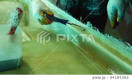 Close-up of a man working on the fiberglass treatment of the boat's hull. Construction of fiberglass pedal catamarans in a private shop. Close-up of a man working on the fiberglass treatment of the boat's hull. Construction of fiberglass pedal catamarans in a private shop. 94165363