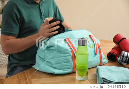 Man packing sports bag for training indoors, closeup 94166510