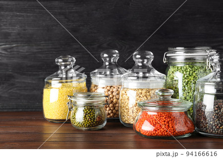 Different types of legumes and cereals in glass jars on wooden table. Organic grains 94166616