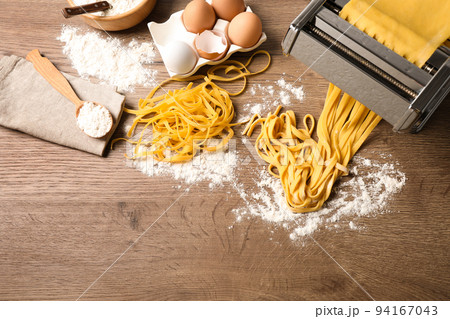 Pasta maker machine with dough and products on wooden table, above view. Space for text Pasta maker machine with dough and products on wooden table, above view. Space for text 94167043