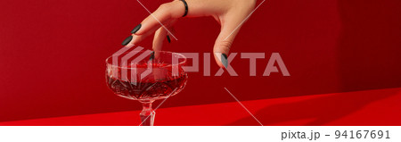 Womans hand with spooky nail design take glass with cranberry halloween cocktail on red background Womans hand with spooky nail design take glass with cranberry halloween cocktail on red background 94167691