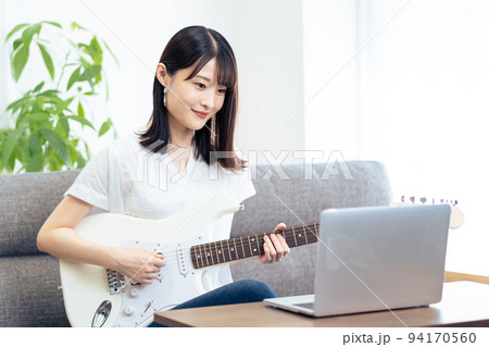 パソコンを見ながら、ギターを弾く女性 94170560