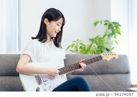 ソファに座りギターを弾く女性 ソファに座りギターを弾く女性 94174097