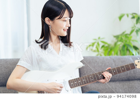 ソファに座りギターを弾く女性 ソファに座りギターを弾く女性 94174098
