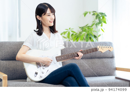 ソファに座りギターを弾く女性 ソファに座りギターを弾く女性 94174099