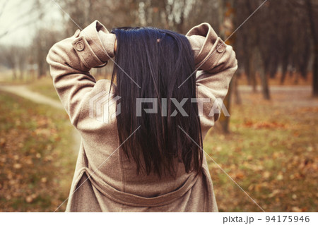 portrait of brunette hair woman in beige coat walking at the city park . 94175946