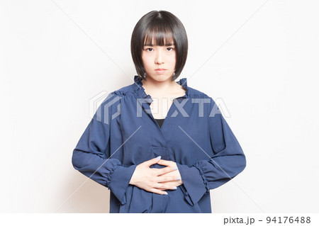白背景の前で、お腹に手を当てる若い女性 94176488