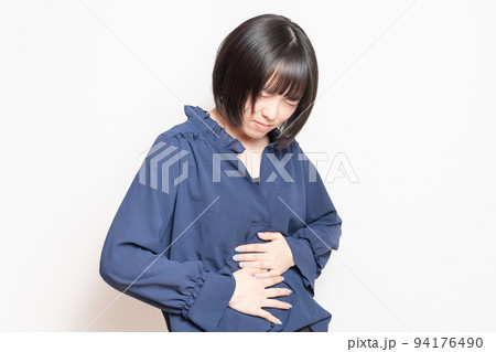 白背景の前で、お腹に手を当てる若い女性 94176490