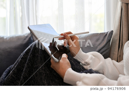 Close-up image, A female relaxes in the living room, sits on sofa and uses a digital tablet. Close-up image, A female relaxes in the living room, sits on sofa and uses a digital tablet. 94176906