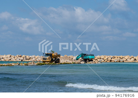 An excavator and a mining truck move stones into the sea. Construction of breakwaters to protect the beach in Netanya in Israel. 94176916
