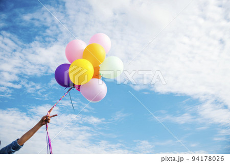 Cheerful cute girl holding balloons running on green meadow white cloud and blue sky with happiness. Hands holding vibrant air balloons play on birthday party happy times summer on sunlight outdoor Cheerful cute girl holding balloons running on green meadow white cloud and blue sky with happiness. Hands holding vibrant air balloons play on birthday party happy times summer on sunlight outdoor 94178026